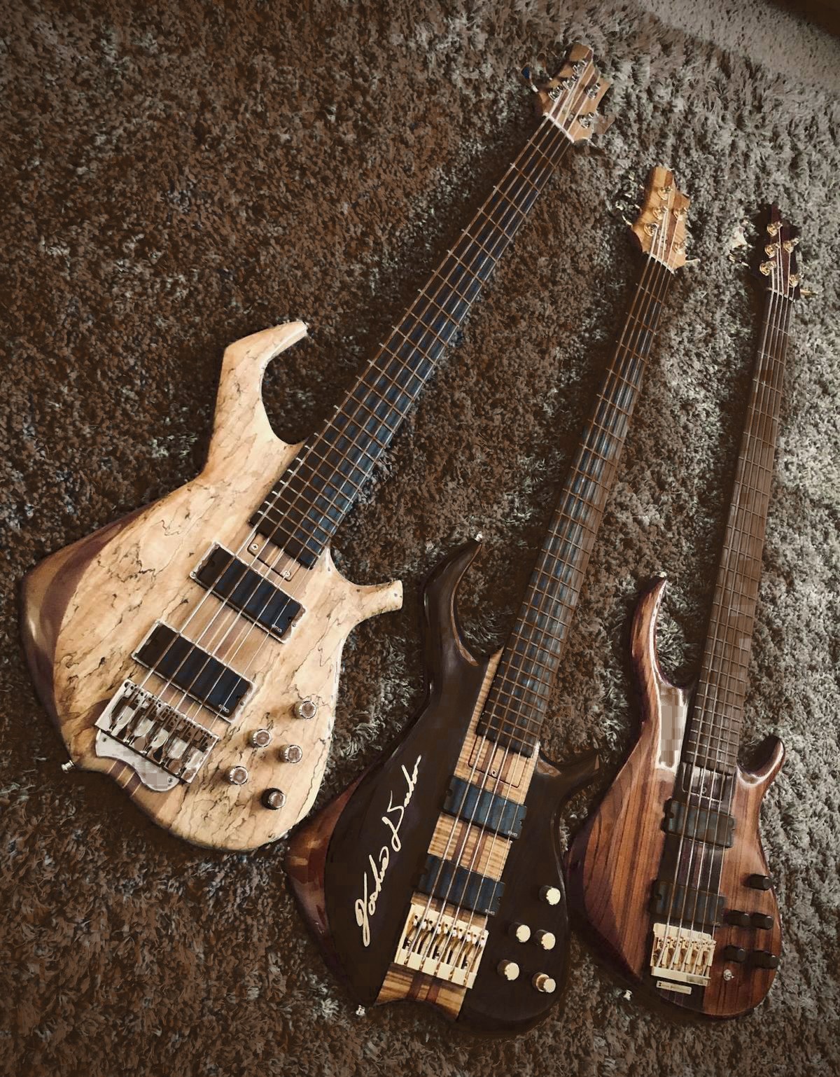 Three custom basses on a dark wood surface
